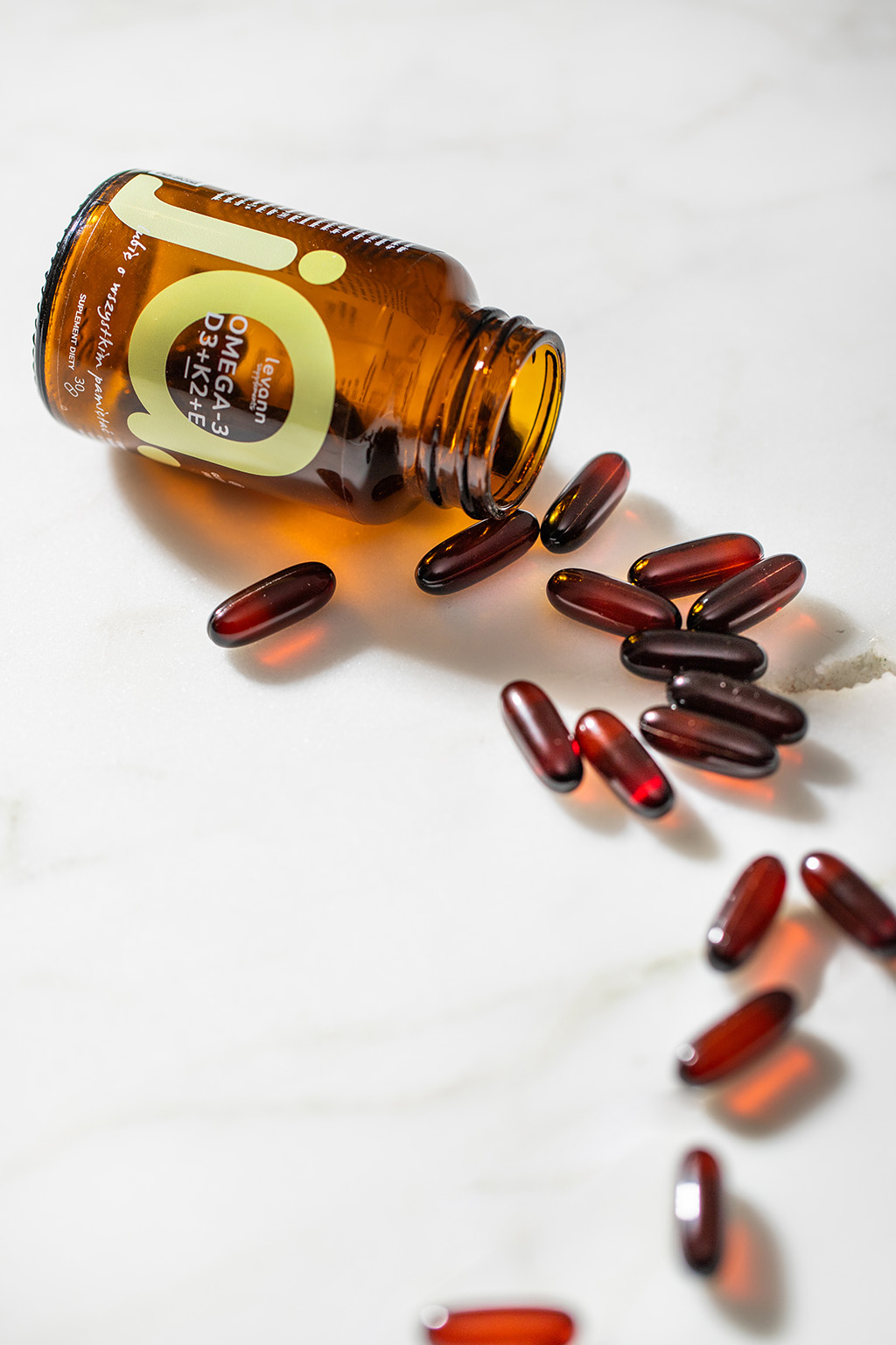 Butelka suplementu marki levann suplements omega-3, przewrócona, z kapsułkami rozsypanymi na marmurowej powierzchni. - zdjęcie