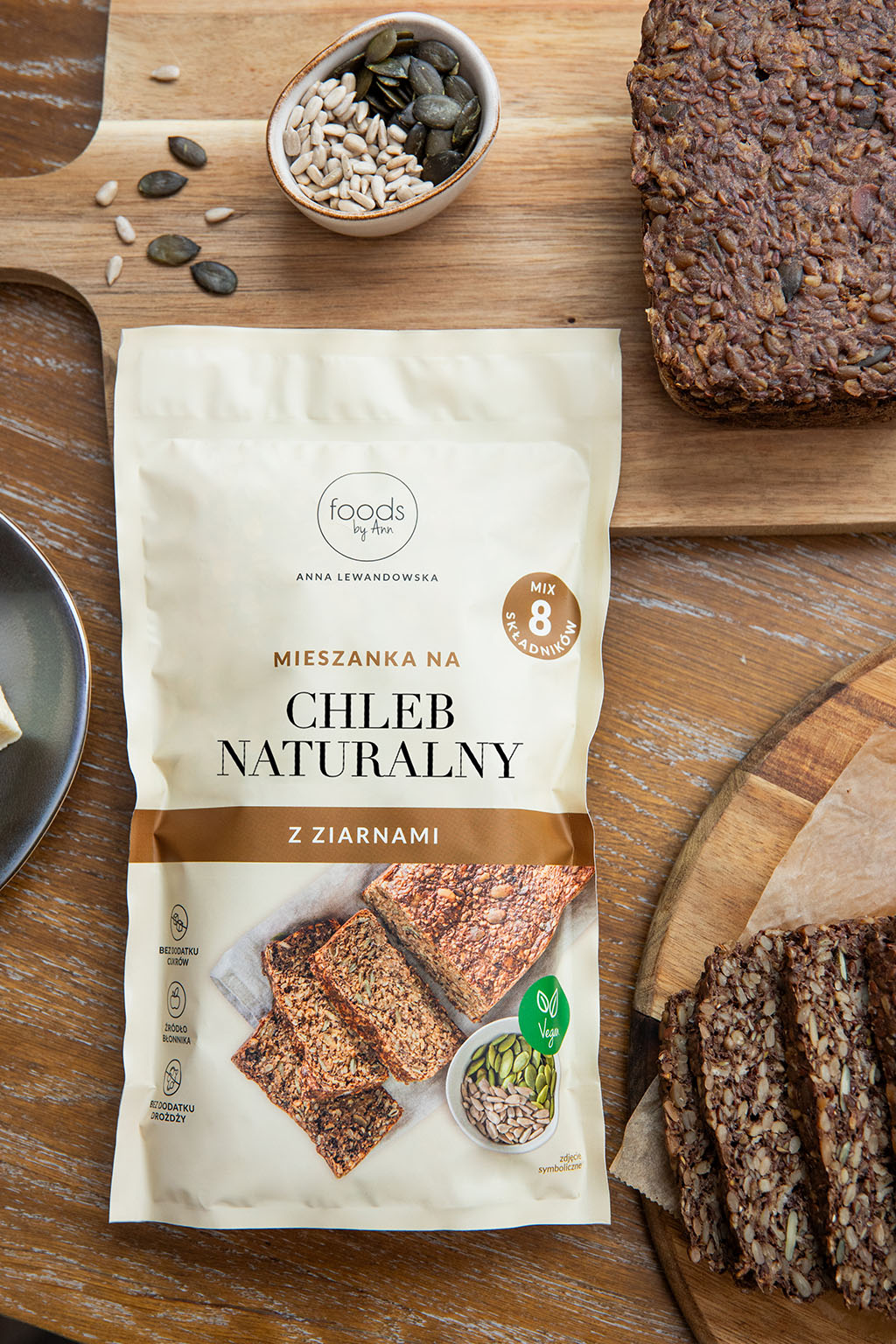 Opakowanie mieszanki na chleb naturalny z ziarnami marki foods by ann obok kawałków świeżo upieczonego chleba z pestkami dyni i słonecznika. - zdjęci